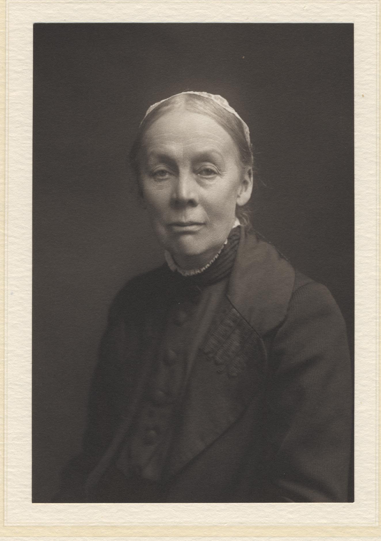Photograph of a woman facing the camera. She is not smiling. She is wearing dark clothes.
