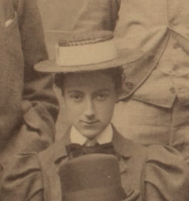 Formal photograph of a womans head and shoulders, facing the camera. She is wearing a boater hat and bow tie. A gentlemans bowler hat is in front of her.