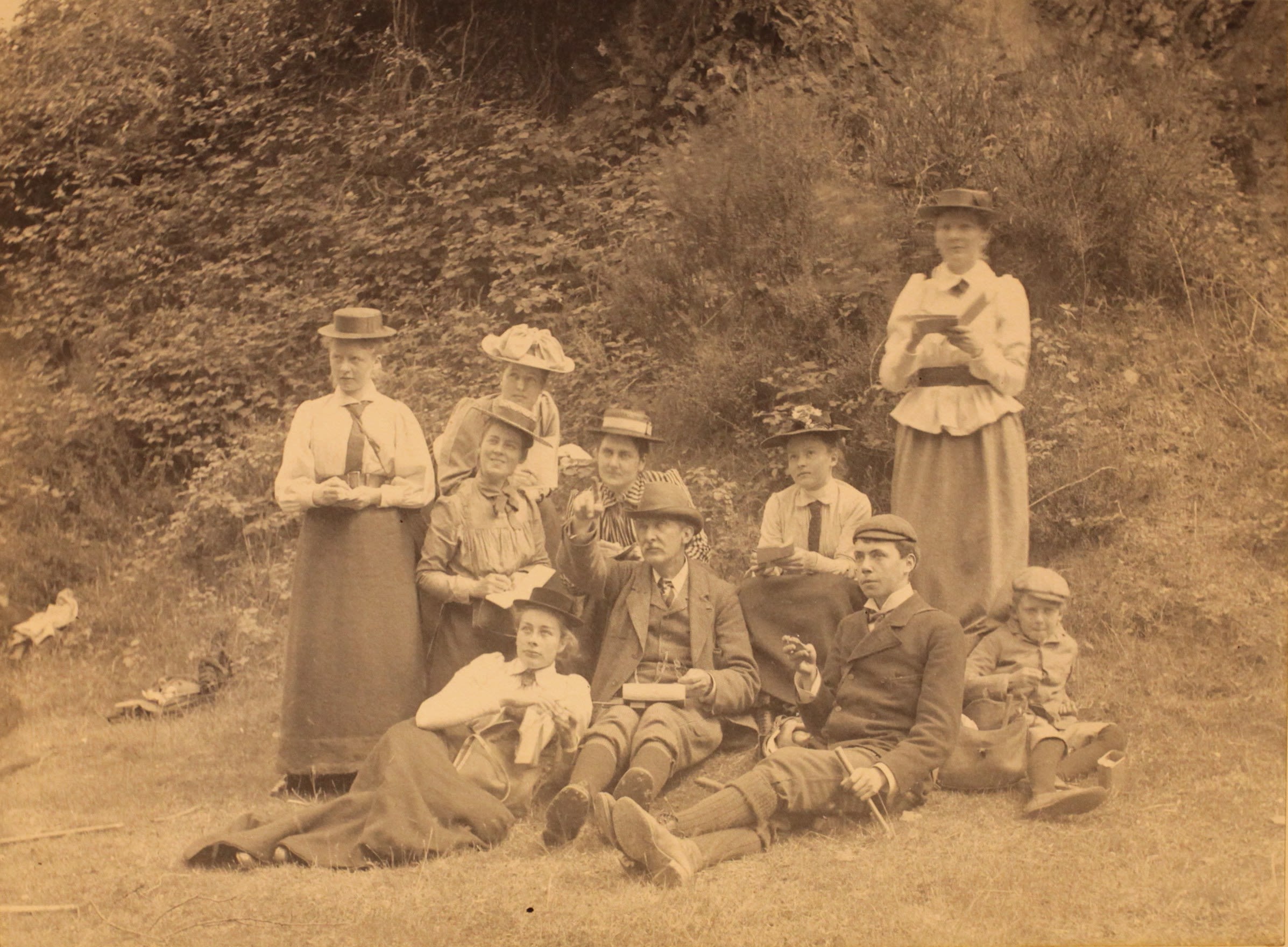 Photograph of students outside making notes. Some are standing, others are sitting down. There is also a male student and a small boy. They are all wearing hats.
