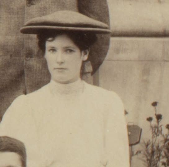 Formal photograph of woman seated outside. She is wearing a large flat cap.