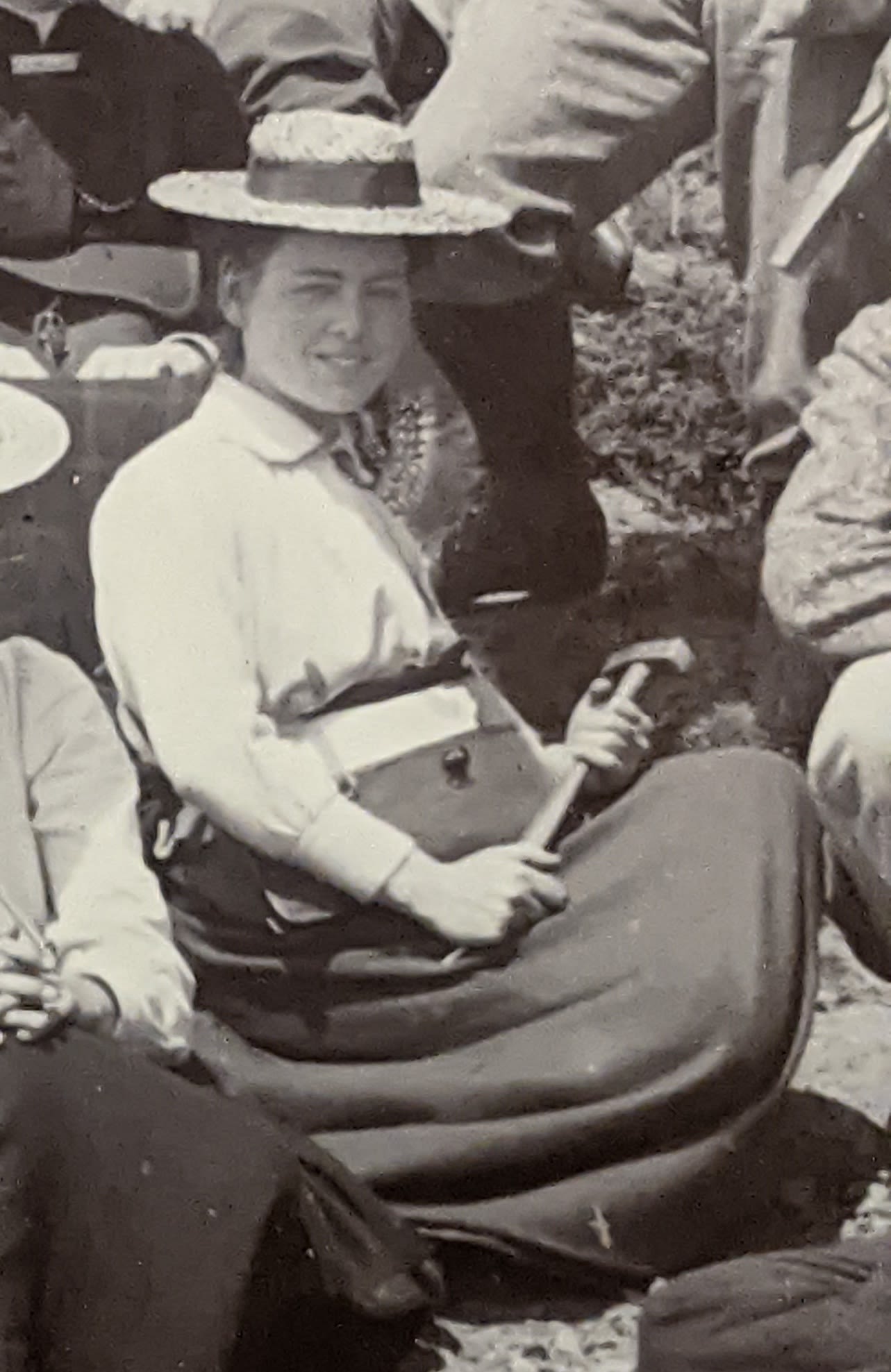 Photograph of a woman seated with notebook and pencil. She is wearing a hat and smiling.