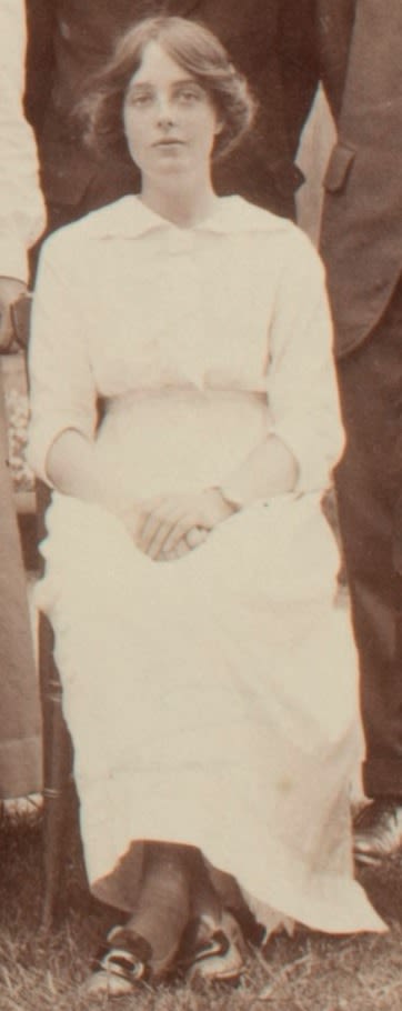 Formal photograph of woman seated outside. She has her hands in her lap.